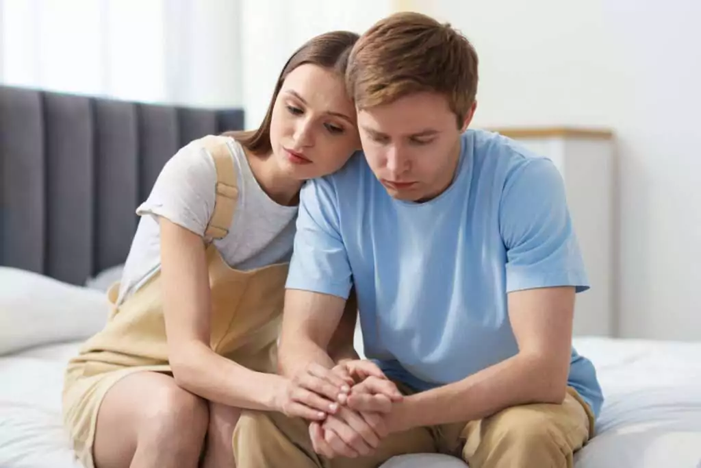 A couple sitting together looking sad and holding hands while coping with the emotional weight of infertility.